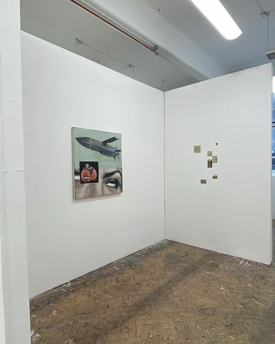 A wider view of the studio gallery: the painting visible on the left wall, with a constellation of smaller works arranged on the partition beyond, daylight filtering through a far window