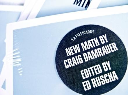 A white postcard box sealed with a black circular label: 12 Postcards / New Math by Craig Damrauer / Edited by Ed Ruscha — conceptual art distilled to pocket format