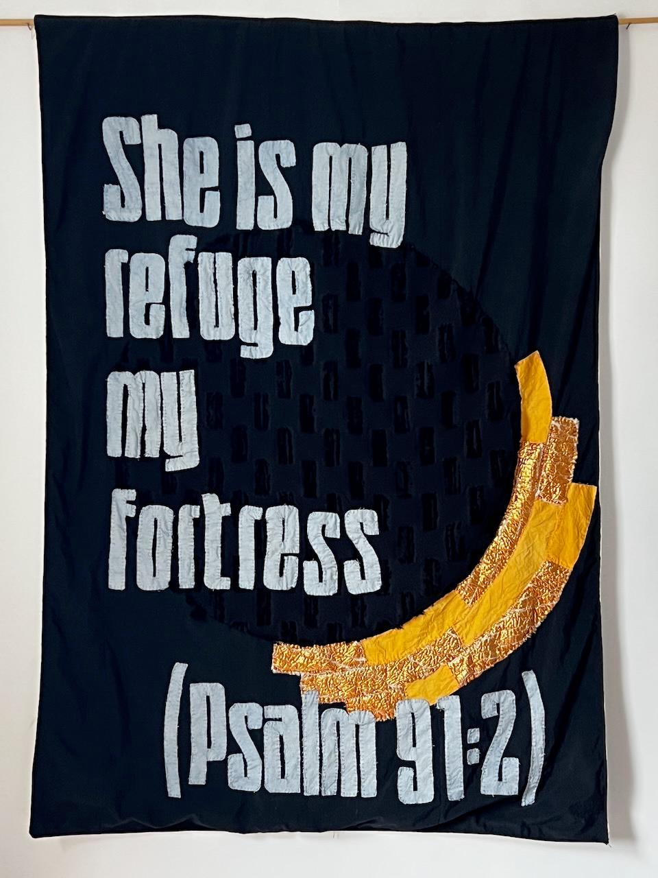 White appliquéd letters on black fabric read 'She is my refuge my fortress (Psalm 91:2)', a golden crescent moon glowing in the lower corner — the feminine divine invoked through hand-stitched scripture