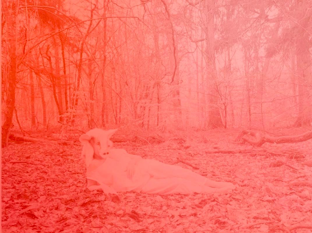 A figure lying in a winter forest wearing a white boar mask and pale garments, the entire scene washed in a spectral pink-red — a phantom reclining among bare trees and fallen leaves